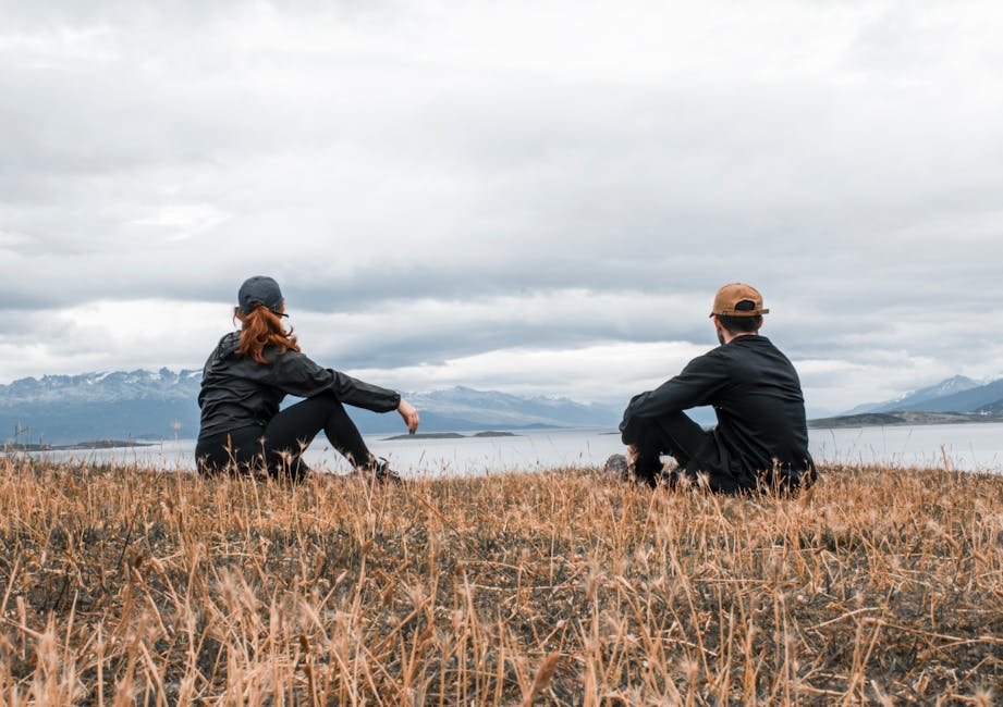 Couple sitting on grass, admiring a lake in Ushuaia, Argentina.