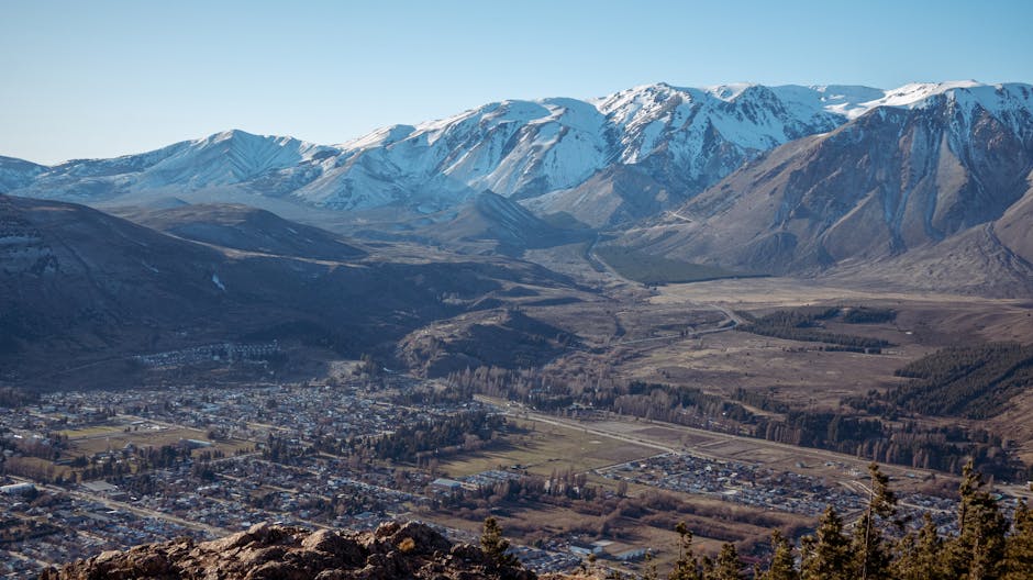 Breathtaking aerial view of a town against snow-capped mountain backdrop under clear blue sky.
